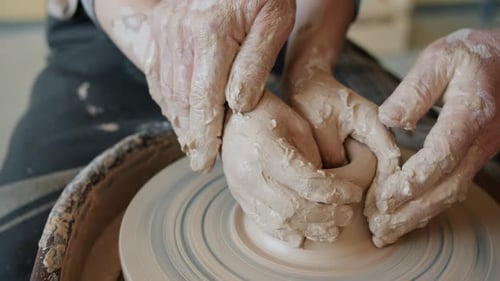 Garçon façonnant de l'argile en vase sur une roue sous la direction d'un potier professionnel
