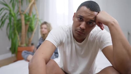 Retrato de un joven afroamericano triste y estresado mirando a la cámara sentado en la cama con Blurred