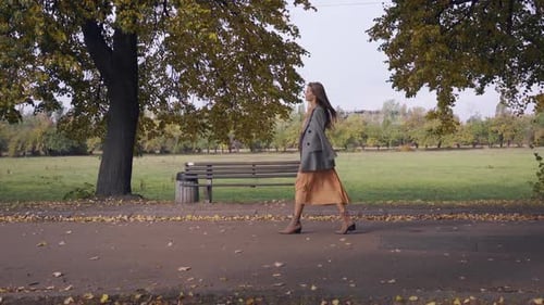 Side View of an Elegant Caucasian Woman in Checkered Jacket and Mustard Dress Strolling Along the