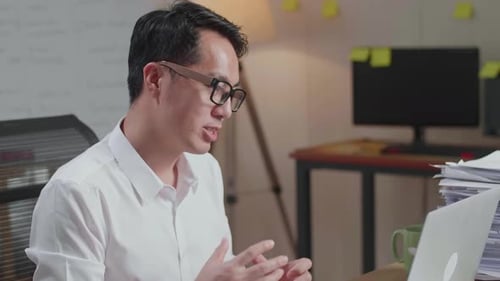 Close Up Of Asian Man Having Video Call On Laptop While Working With Documents At The Office