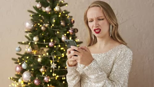 Woman Frowning at Phone Next to Christmas Tree