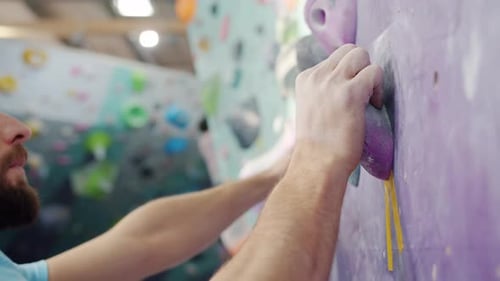 Close-up of Strong Young Man Moving Up Artificial Climbing Wall in Indoor Center