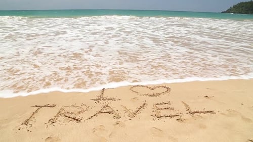 I LOVE TRAVEL geschrieben im Strandsand, der von Wellen weggespült wird.