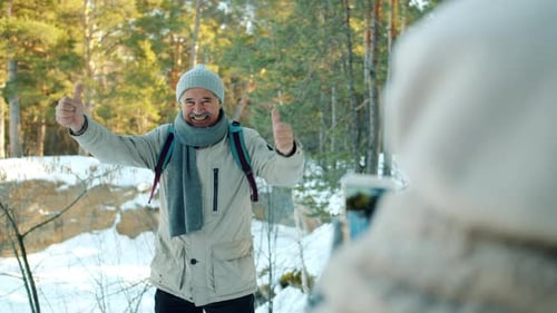 Happy Elderly Man Tourist Posing for Smartphone Camera Showing Thumbs-up Gesture in Forest in Winter