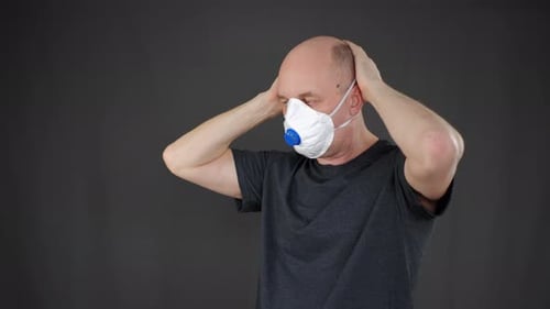 Man Puts on a White Disposable Respirator Mask