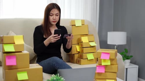 woman entrepreneur using a smartphone with credit card at home office, (SME business)