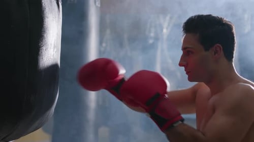 Young Male Boxer Hitting Punching Bag in Gym