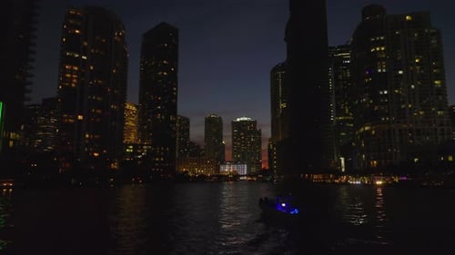Low Forwards Fly Above Water Surface Between Silhouettes on High Rise Downtown Buildings on Banks
