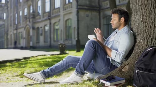 Thoughtful Student Writing Under Tree on University Campus