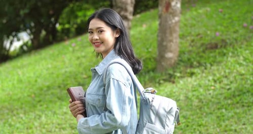 Young Woman Smiling Outdoors Holding Book and Backpack