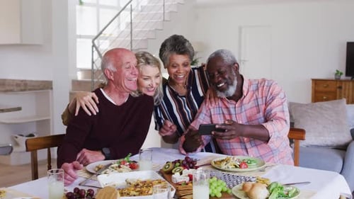 Cheerful Friends Gathering Around Table Looking at Phone