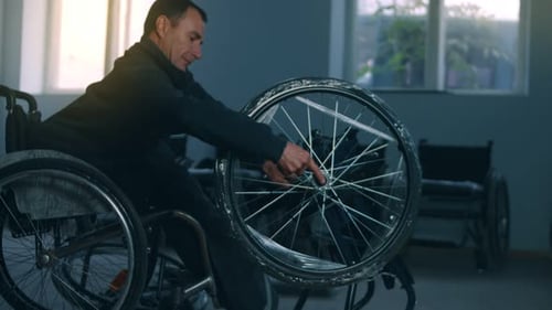 Side View of One American Male Workers in a Workshop at a Factory Making Wheelchairs Sitting at a