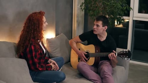 Man Plays Guitar for Young Woman on Couch