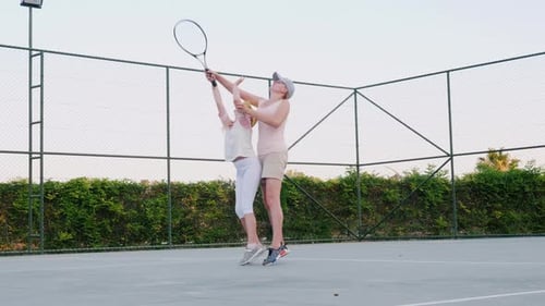 Child Learns Tennis Swing With Adult Supervision on Court