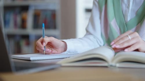 Hände eines Schülers, der Hausaufgaben in der Bibliothek macht