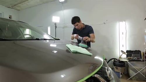 Man Polishing Car Hood With Machine In Garage