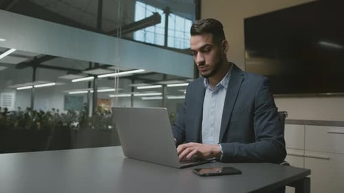 Young Concentrated Arab Man Office Worker Typing on Laptop Making Research in Internet or Financial