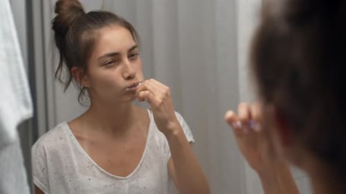 Woman Brushing Teeth in Bathroom Mirror