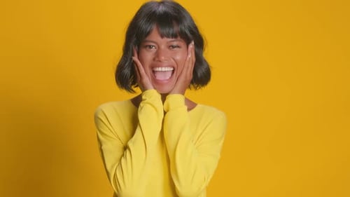 Woman Smiling With Hands on Cheeks on Yellow Backdrop
