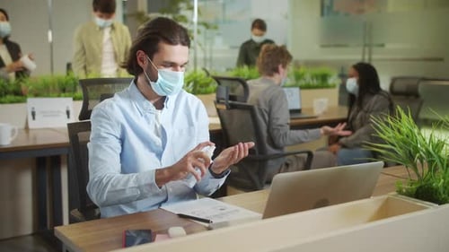 Man Uses Hand Sanitizer at Desk in Office