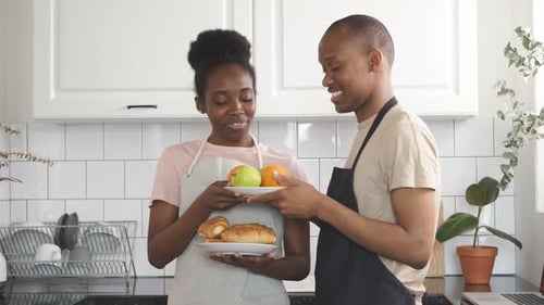 Smiling Couple in Kitchen Hold Plates of Food