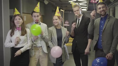 Cinco funcionários de escritório caucasianos positivos em chapéus de festa olhando para a câmera e sorrindo em espaço aberto