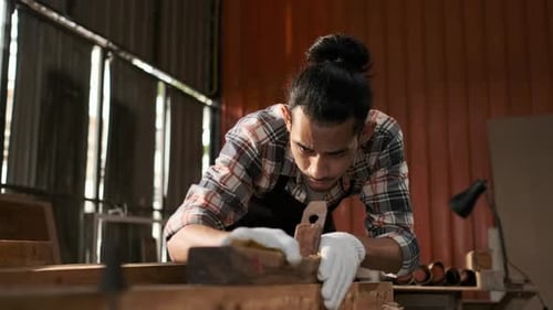 Woodworker planes a piece of wood in workshop