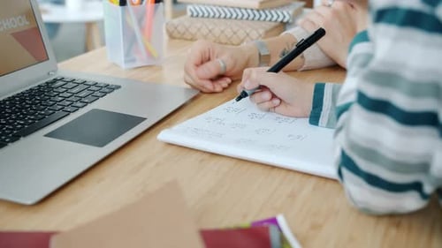 Child Writes in Notebook with Adult Teacher