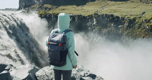 Frau steht am Rand der Klippe mit Blick auf den Detifoss-Wasserfall und den Canyon in Island
