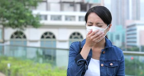 Woman Coughs While Wearing a Mask in City