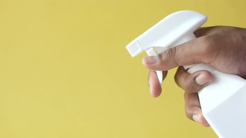 Hand Sprays White Bottle on Yellow Background