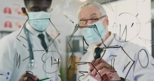 Des médecins de race mixte portant des masques médicaux stériles discutant d'une formule chimique dessinée sur ce mur