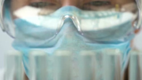 Asistente de laboratorio haciendo análisis químicos, tubos de ensayo que se reflejan en gafas
