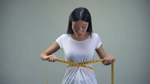 Femme asiatique mesurant sa taille, satisfaite des résultats de l'entraînement et de l'alimentation, en forme