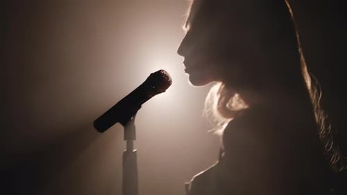Close-up of the Face of the Singer with Microphone on a Black Smoky Background. The Singer Sings a