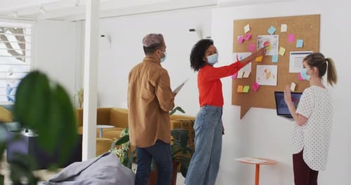 Woman wearing face mask discussing over memo notes with her colleagues at office