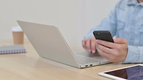 Mann benutzt Laptop mit Smartphone