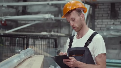 Fabrikmann überprüft Pappkarton und schaut auf die Zwischenablage im Lagerhaus