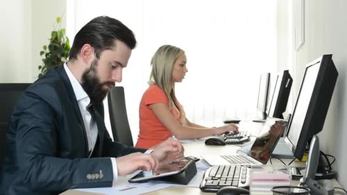 Man Works on Tablet and Woman Works on Desktop Computer in the Office (Workers)