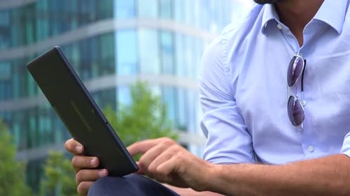 Ein junger gutaussehender Geschäftsmann arbeitet auf einem Tablet - Nahaufnahme - ein Bürogebäude im Hintergrund