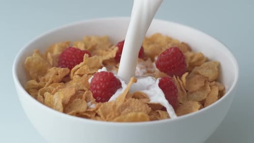 Milk Pouring Over Cereal and Raspberries in Bowl