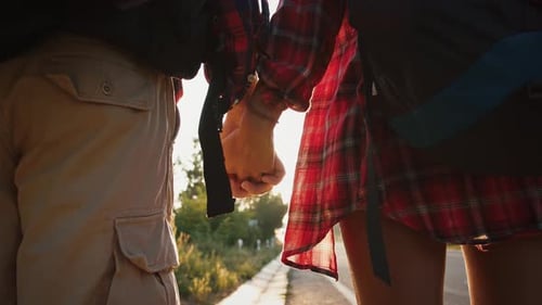 Two Travellers Holding Hands and Walking Along Road Towards Sunset