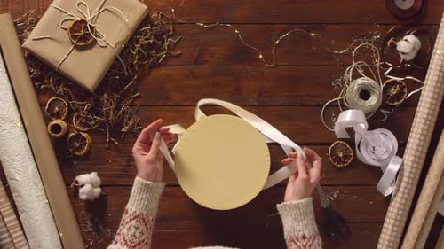 Woman Wrapping Christmas Present with White Ribbon