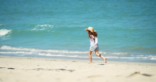 A Funny Little Girl in a Hat Runs Along the Shore Along the Beach a Child on a Sunny Day By the Sea