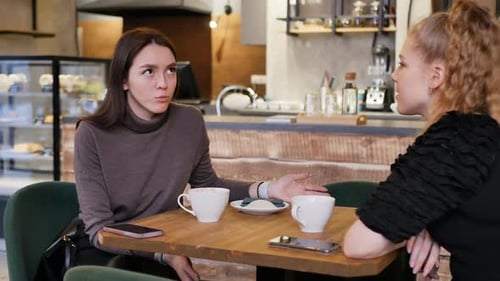 Junge Blondine und Brünette an einem Tisch in einem Restaurant reden und trinken Tee