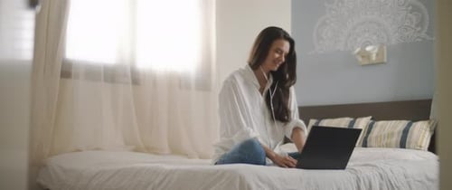 Woman on Bed Using Laptop with Headphones