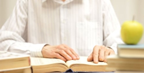 Adult Reading a Book With Apple at Desk