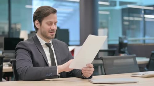 Excited Businessman Reviewing Documents in Modern Office