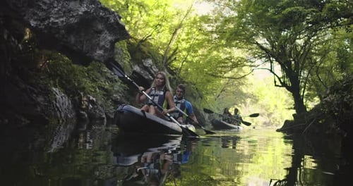 People Kayaking Down Serene River in Green Forest