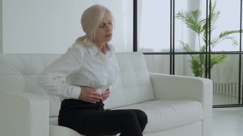 Woman Sitting on Couch with Stomach Pain
